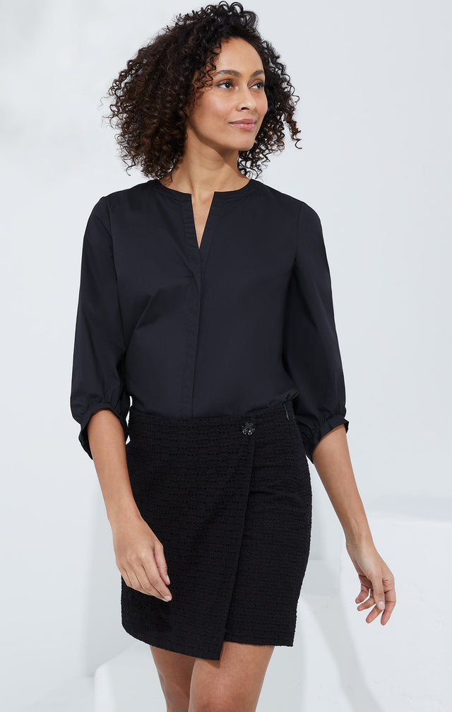 Lookbook photo of a model wearing the Doyenne shirt, which is a stretch cotton black blouse.